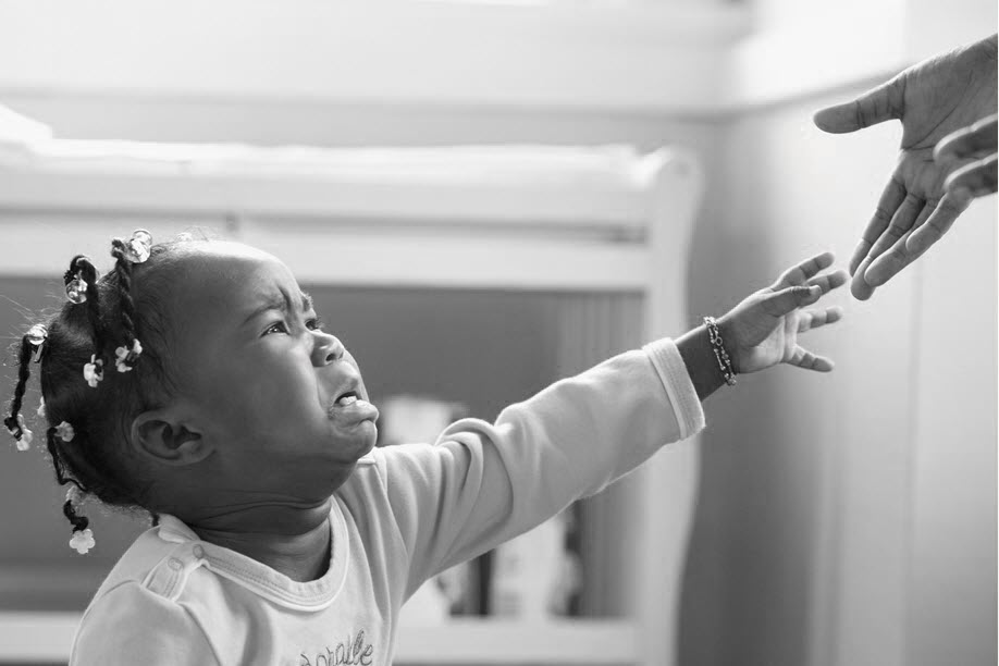 A crying young child reaching toward an adult's hand