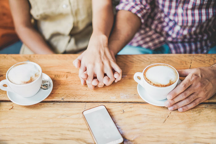 A married couple lovingly taling to each other over two cups of coffee. Phone down.